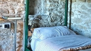 A bunk bed in a rustic stone-walled room with a metal table and a power outlet. - Agriturismo Fattoria Ortoalpino (Borgo Valbelluna)