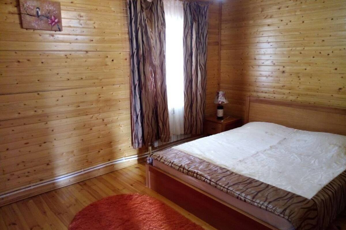 A wooden-paneled room with a bed, a red rug, and a nightstand with a lamp.