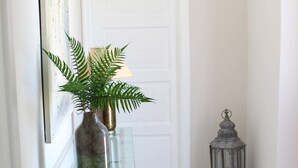 A hallway with a glass table, a potted plant, a lantern, and a white door. - Olympus (Corinth)