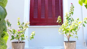 A white building with a red window shutter, two potted plants, and two wall-mounted light fixtures. - Olympus (Corinth)