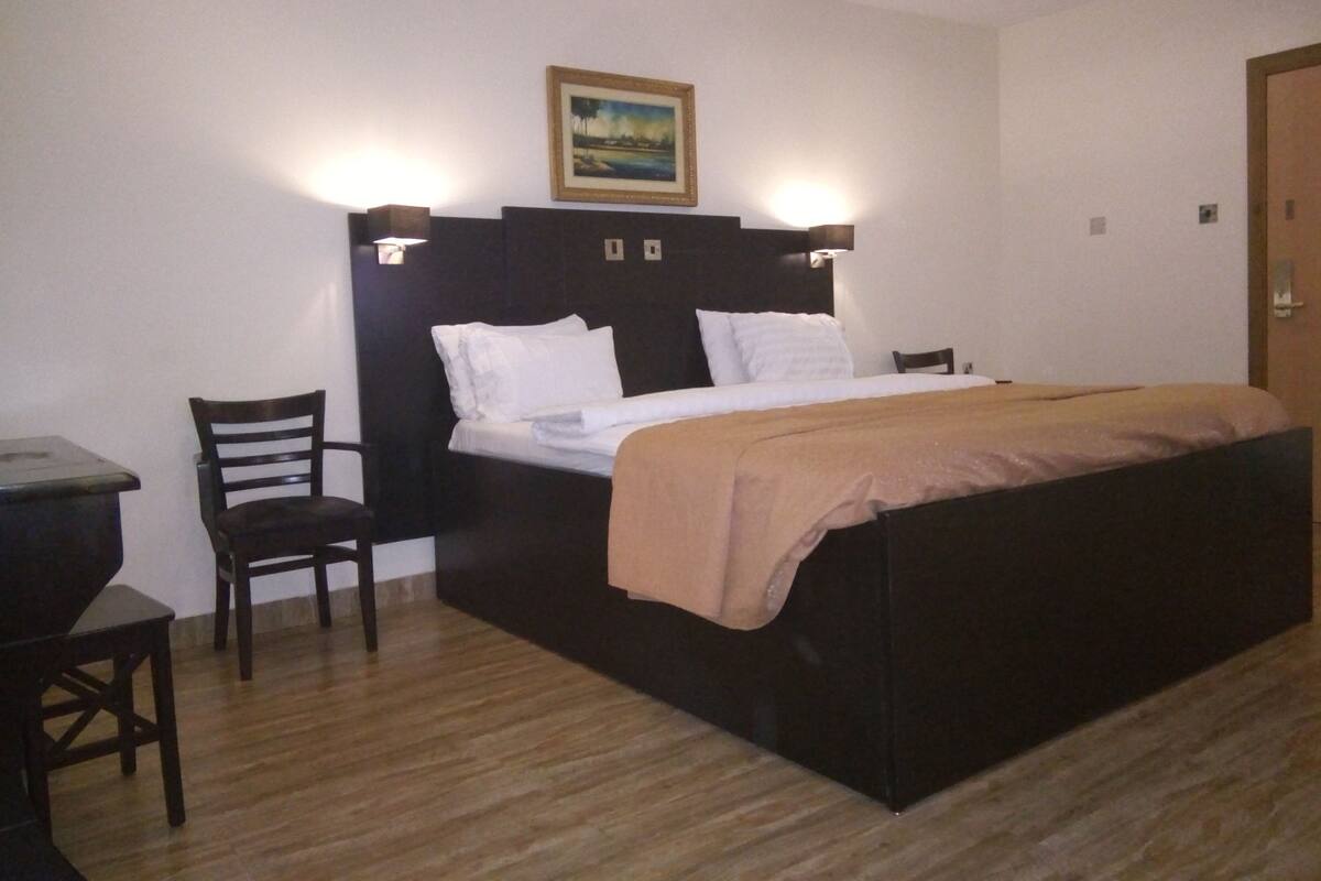 A hotel room with a bed, a chair, a desk, and a painting on the wall.