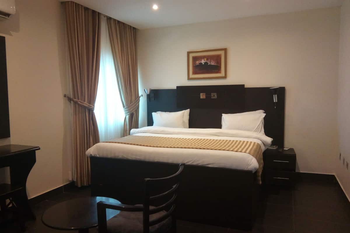 A hotel room with a bed, a desk, a chair, and a painting on the wall.