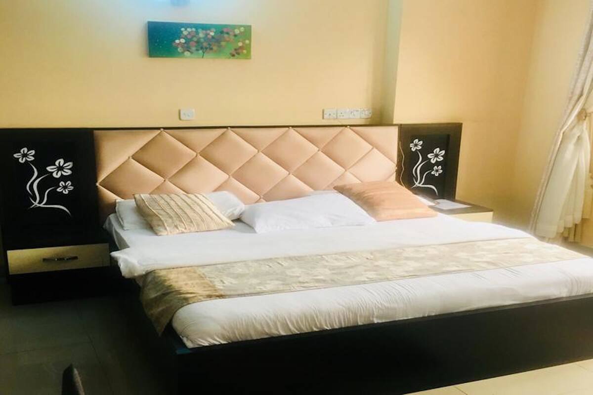 A neatly made bed with a tufted headboard, a bedside table with a drawer, and a wall-mounted artwork above.