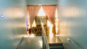 Un escalier menant à une pièce dont le mur est décoré de motifs et qui est agrémentée d’un rideau.