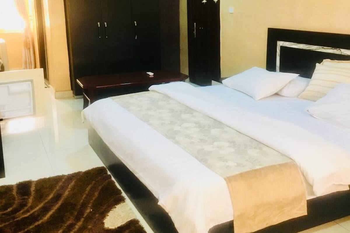 A hotel room with a bed, a wardrobe, a desk, and a rug.