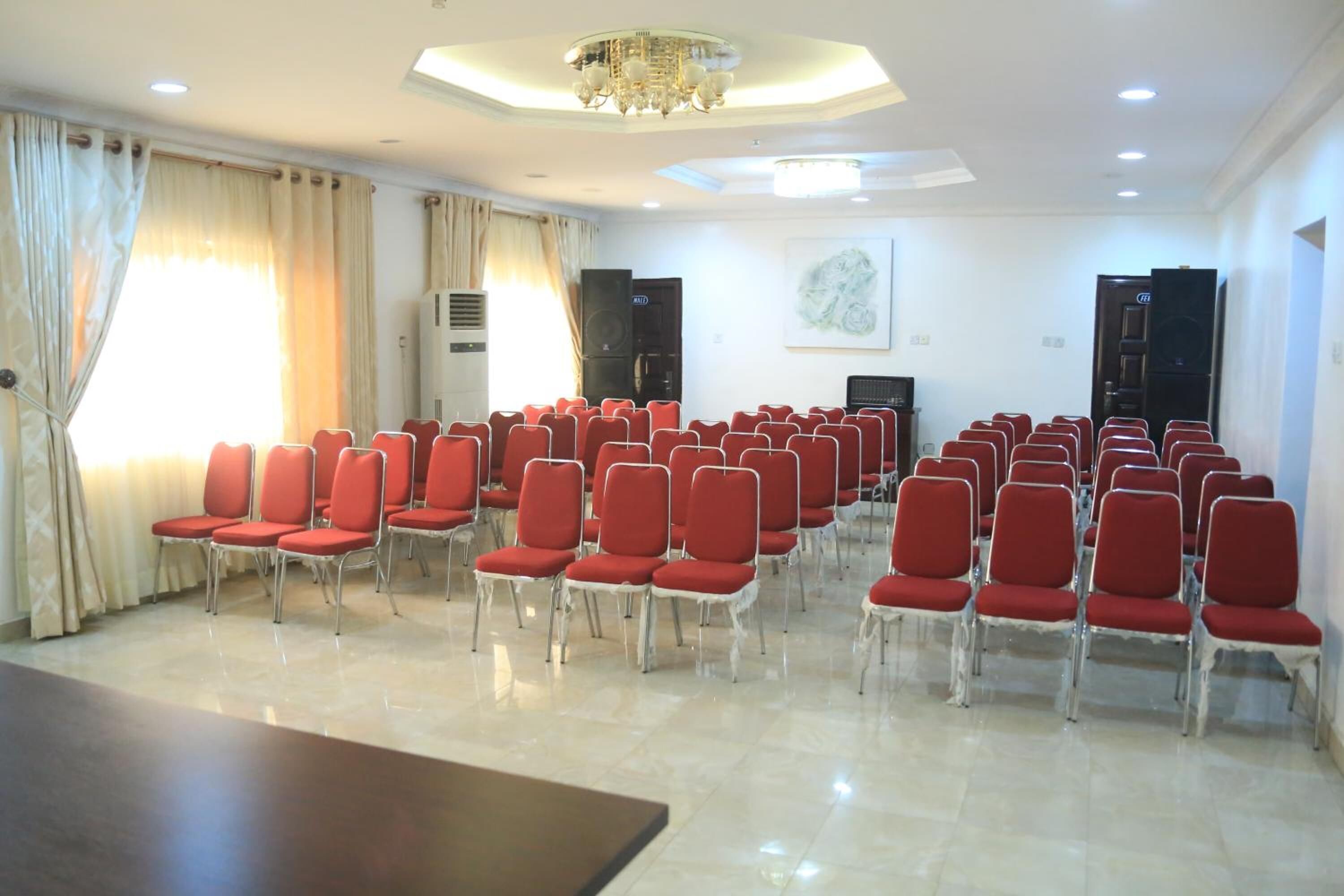 Une salle de conférence avec des rangées de chaises rouges, une grande table et un lustre.