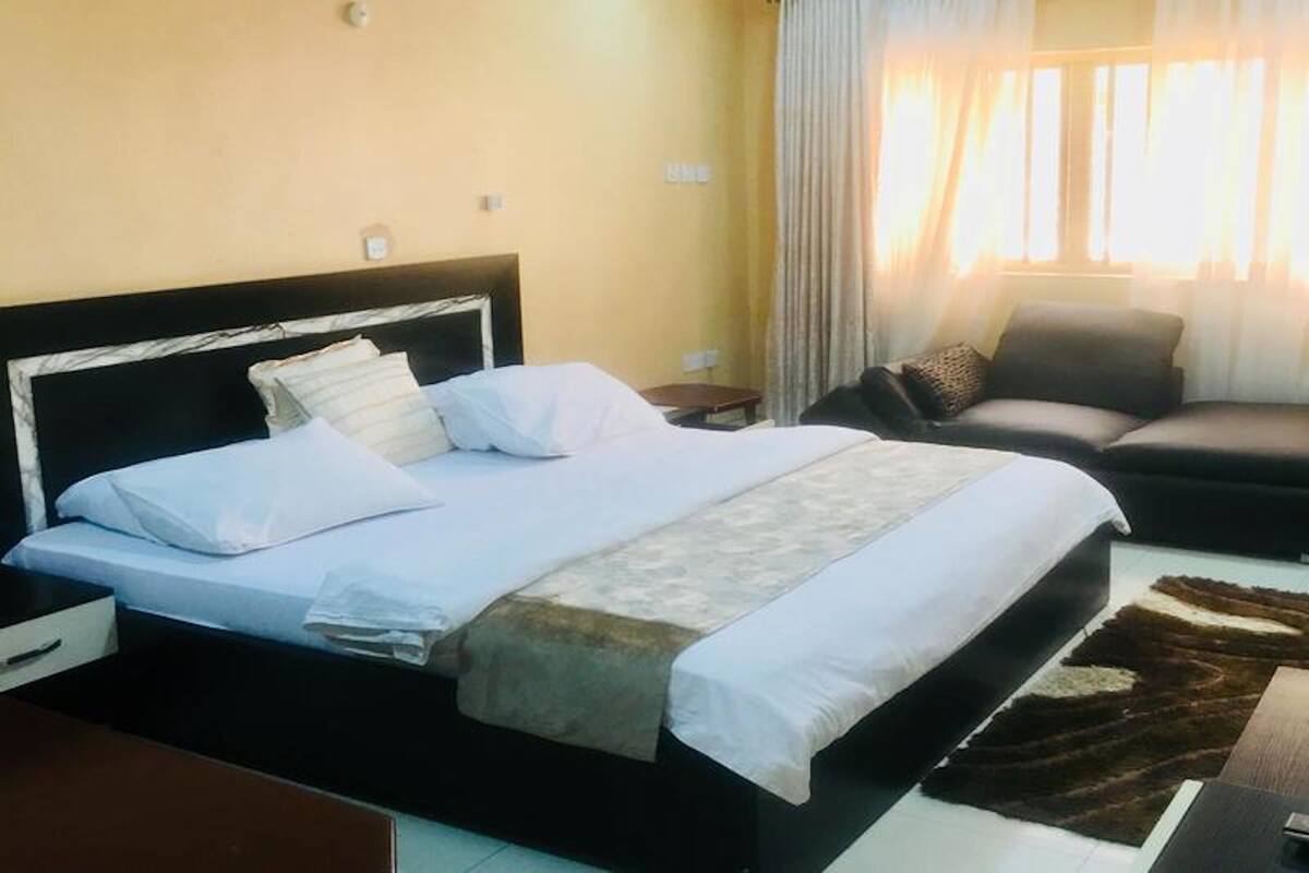 A hotel room with a bed, a sofa, a nightstand, and a window with curtains.
