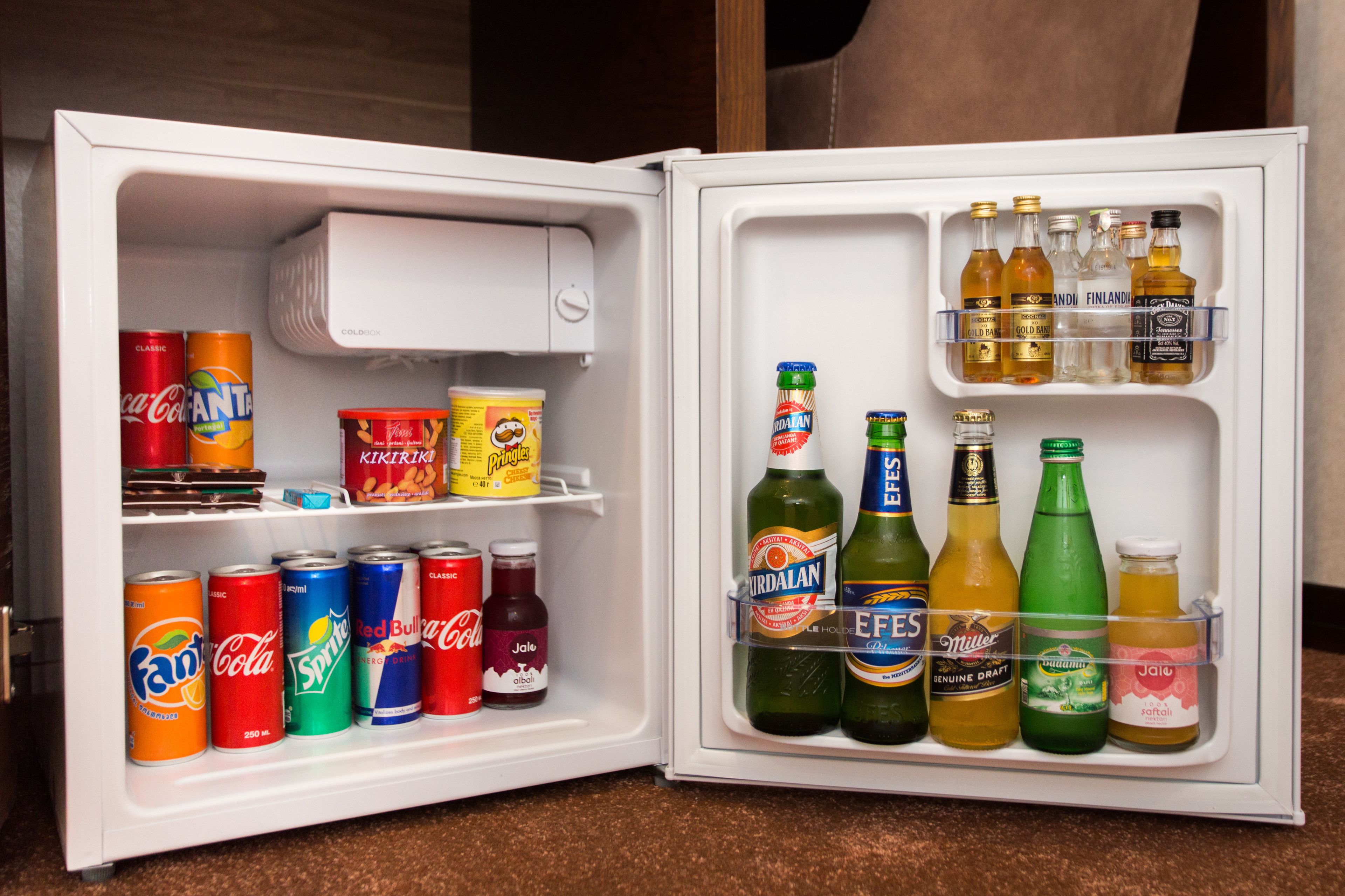 Un refrigerador abierto con diversas bebidas y aperitivos.