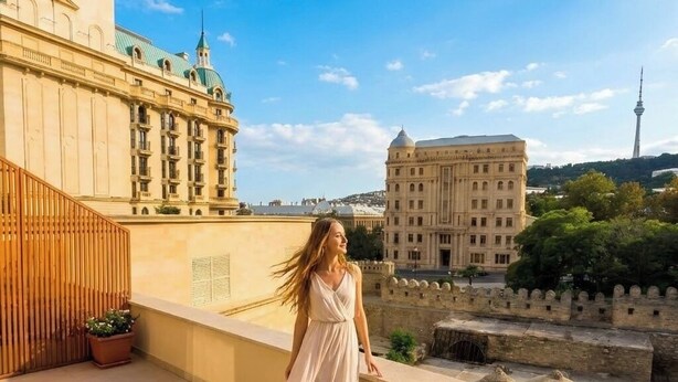 En kvinde står på en balkon med udsigt over en by og historiske bygninger samt et tårn.