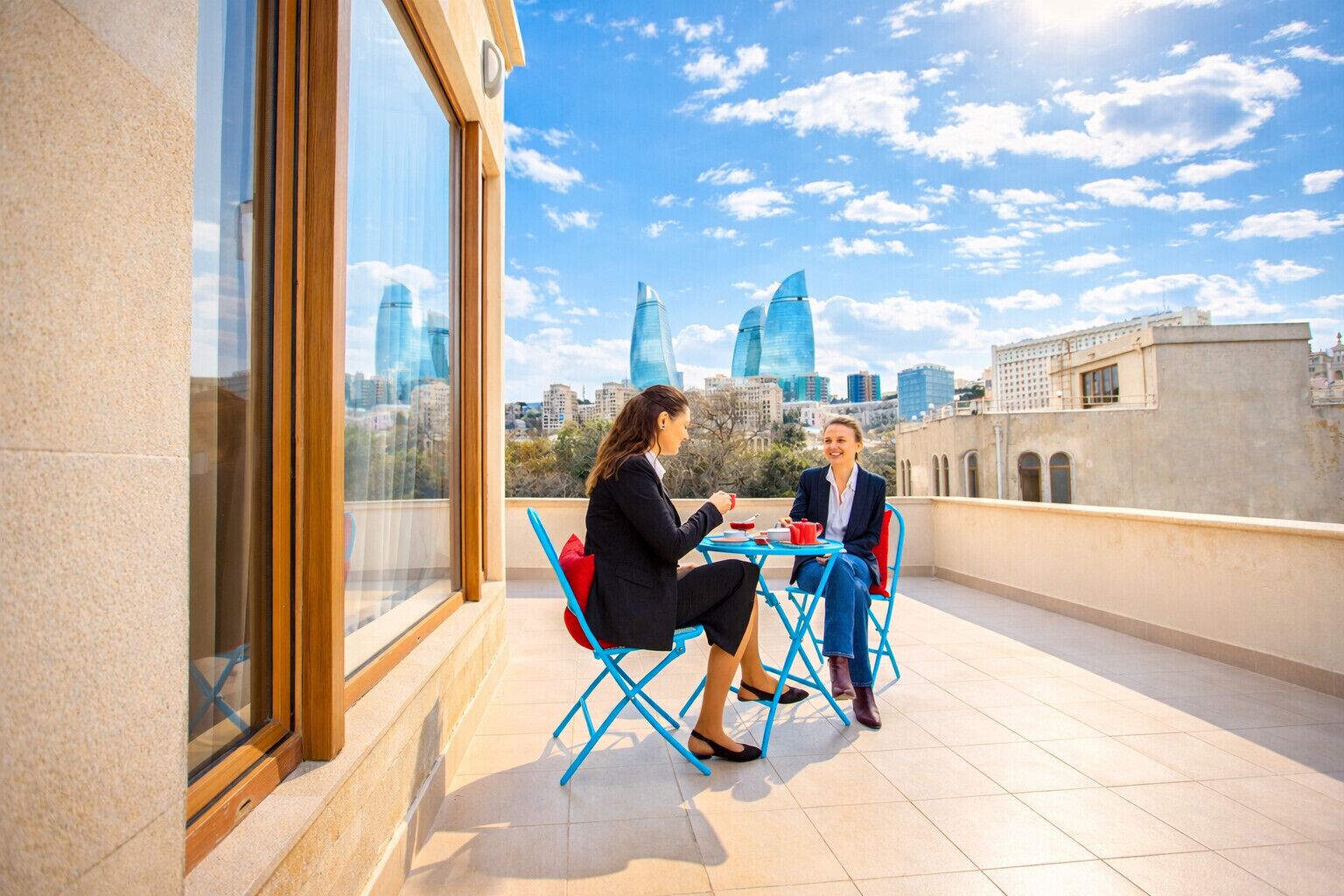 Two people seated at a table on a rooftop terrace with a city skyline in the background.