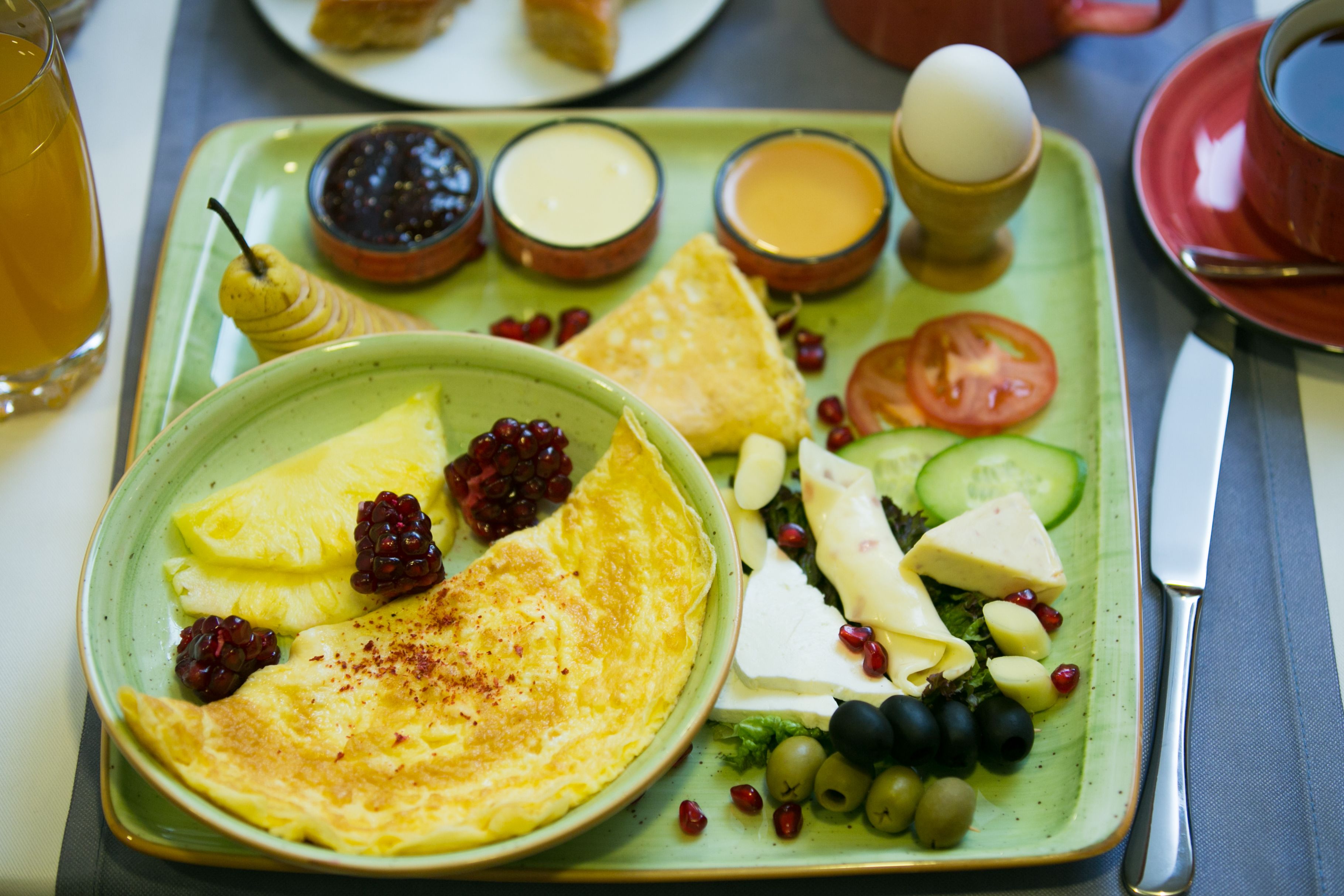 Un plato de desayuno con huevos, queso, tomates, pepinos, aceitunas y bayas.