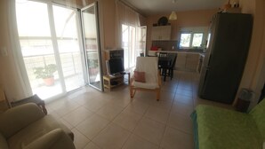 A living room with a sofa, a chair, a TV, and a sliding glass door leading to a balcony. - Kanakaris Apartments (Xylokastro-Evrostina)