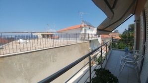 A balcony with a metal railing, a concrete floor, and a view of neighboring buildings and a clear sky. - Kanakaris Apartments (Xylokastro-Evrostina)