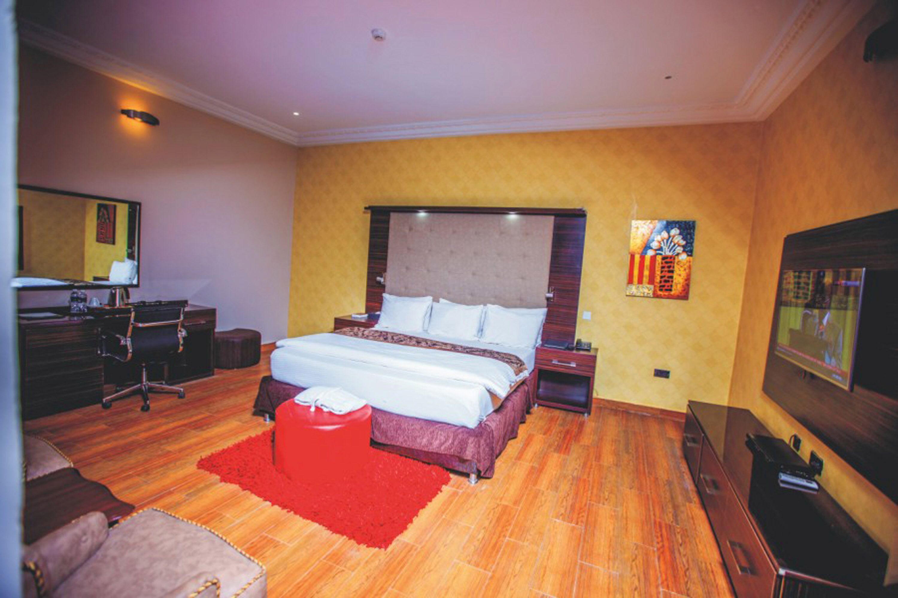 Une chambre d’hôtel avec un grand lit, un bureau, une chaise, une télévision et un tapis rouge.