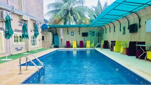 A swimming pool with a tiled deck, surrounded by colorful lounge chairs and umbrellas. - Eterno Hotels Limited (Benin City)