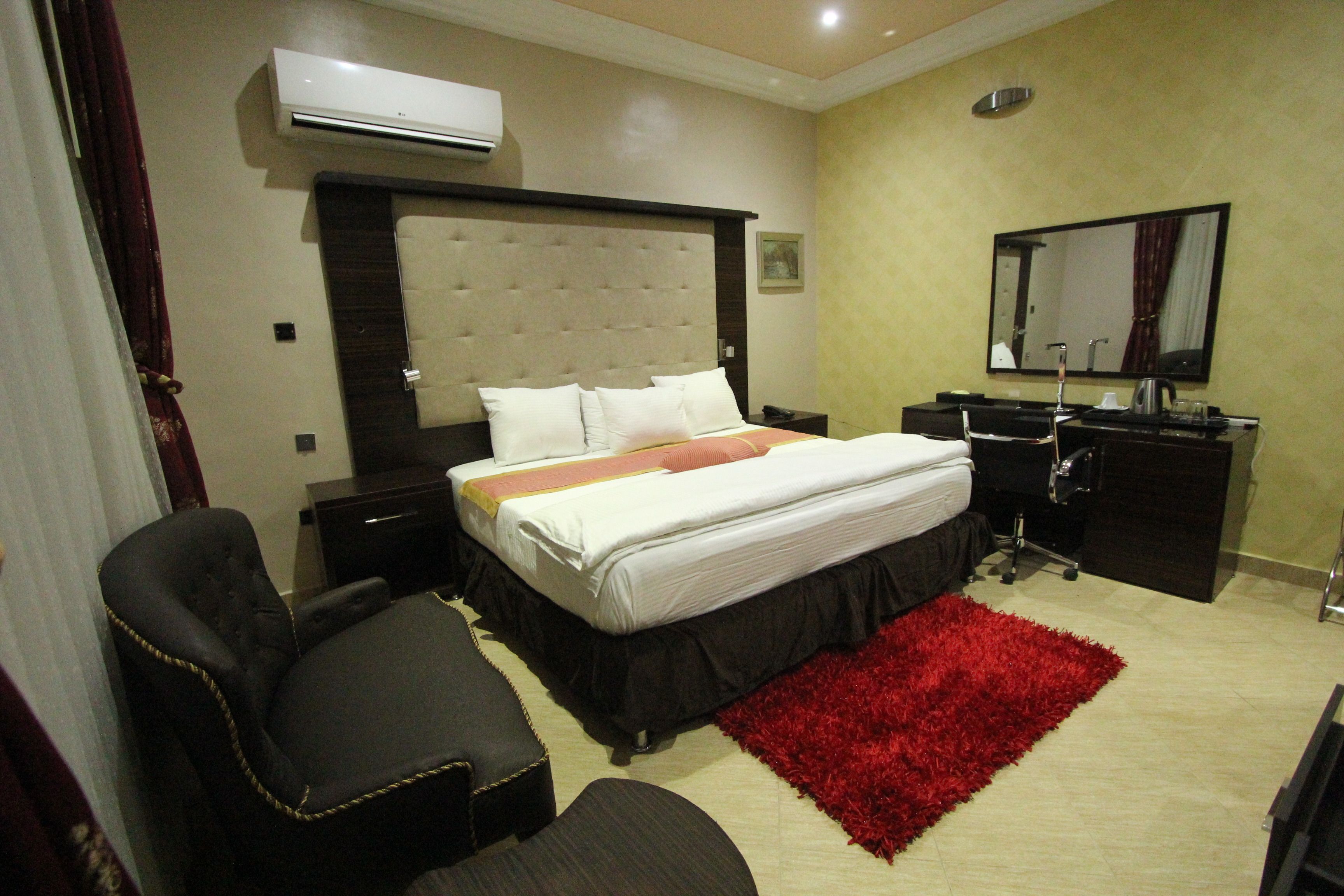 Une chambre d’hôtel avec un grand lit, un tapis rouge, un bureau avec une chaise, une commode et un miroir.