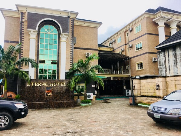 A hotel entrance with a large arched window, a sign reading "L'Terno Hotel," and a paved driveway with parked cars.