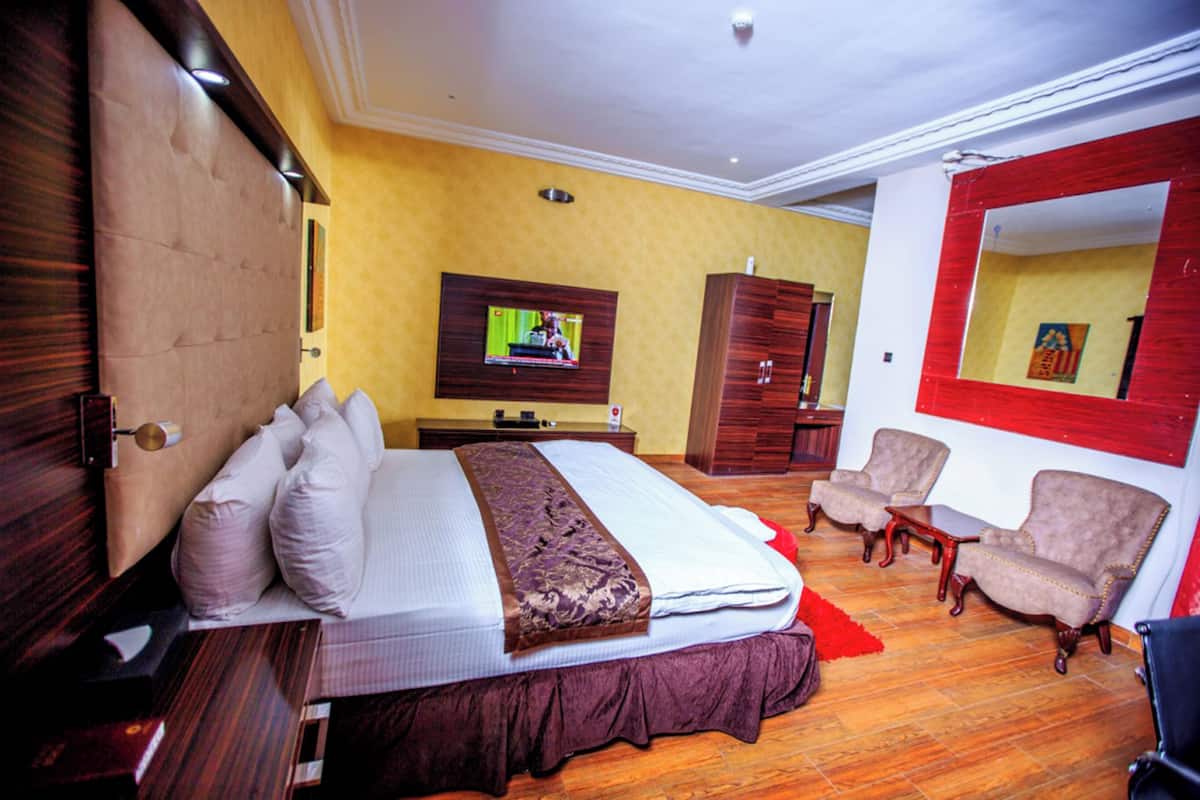 Une chambre d’hôtel avec un grand lit, un téléviseur fixé au mur, une armoire, deux fauteuils et une petite table.
