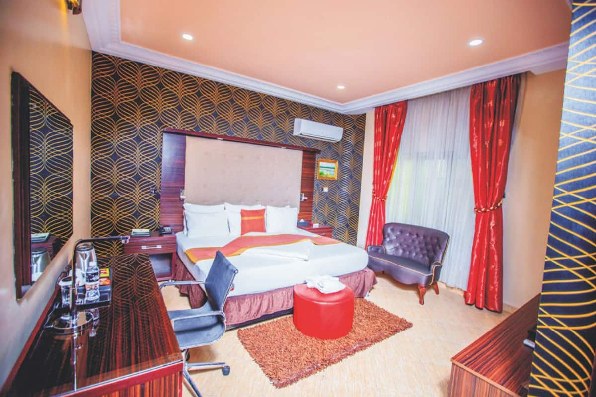 Une chambre d’hôtel avec un grand lit, un bureau avec une chaise, un pouf rouge et un rideau rouge et blanc.