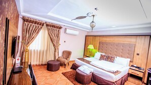 A hotel room with a bed, a chair, a desk, a lamp, and a ceiling fan. - Eterno Hotels Limited (Benin City)