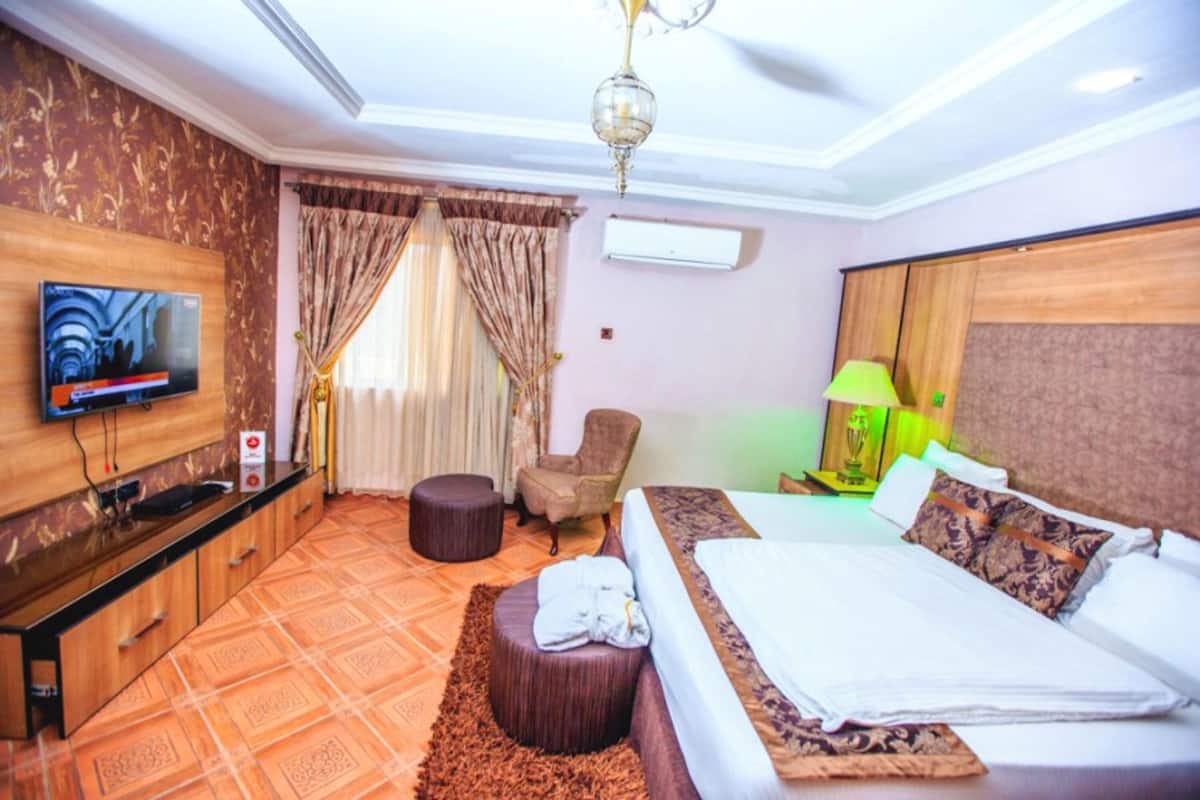 Une chambre d’hôtel avec un lit, une télévision, une chaise, une petite table et une fenêtre avec des rideaux.