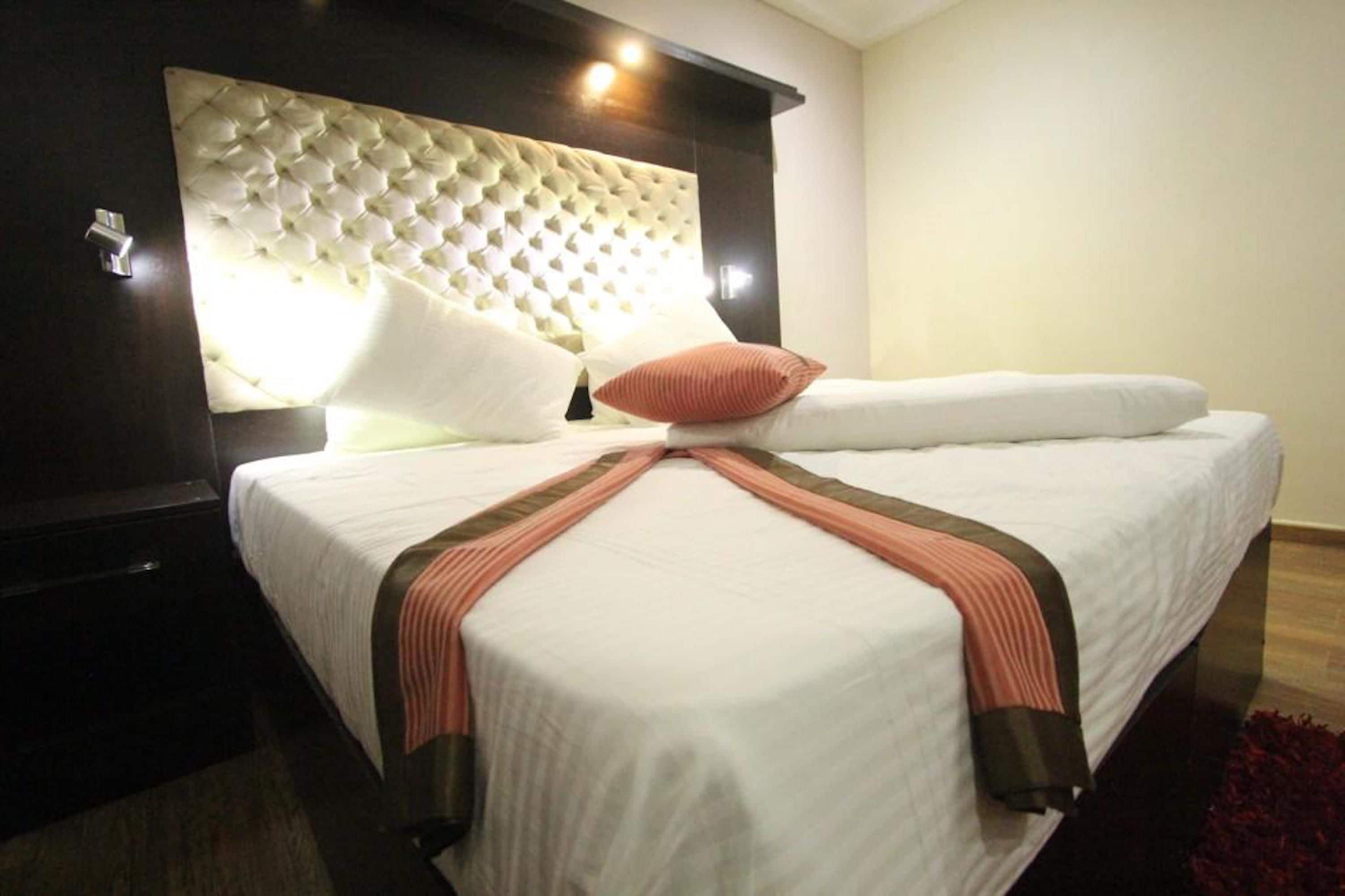 Una cama bien hecha con cabecera tapizada, ropa de cama blanca y un corredor decorativo a rayas rosas y marrones.