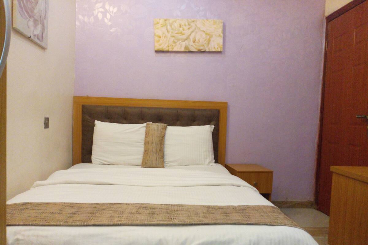 A bed with a wooden headboard, white bedding, and a beige throw blanket.