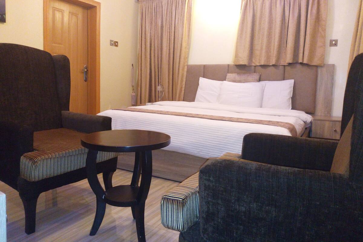 A hotel room with a bed, two armchairs, a small table, and a door.