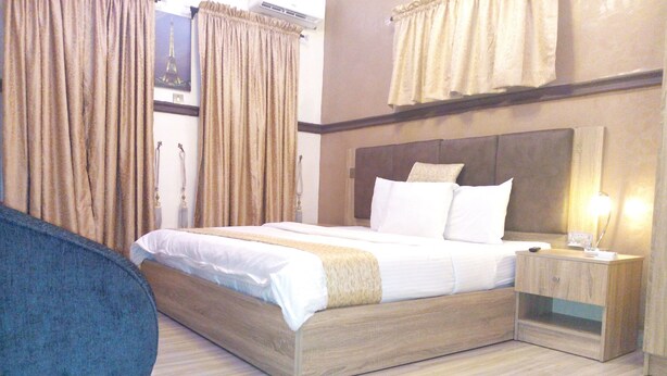 A hotel room with a large bed, a bedside table with a lamp, and curtains. - Euro Lounge and Suites (Ibadan)