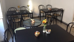 A dining area with round and square tables, black chairs, and a vase with flowers on one table. - Guest House Roma (Genoa)