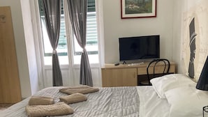 A hotel room with a bed, a desk, a TV, and a window with curtains. - Guest House Roma (Genoa)