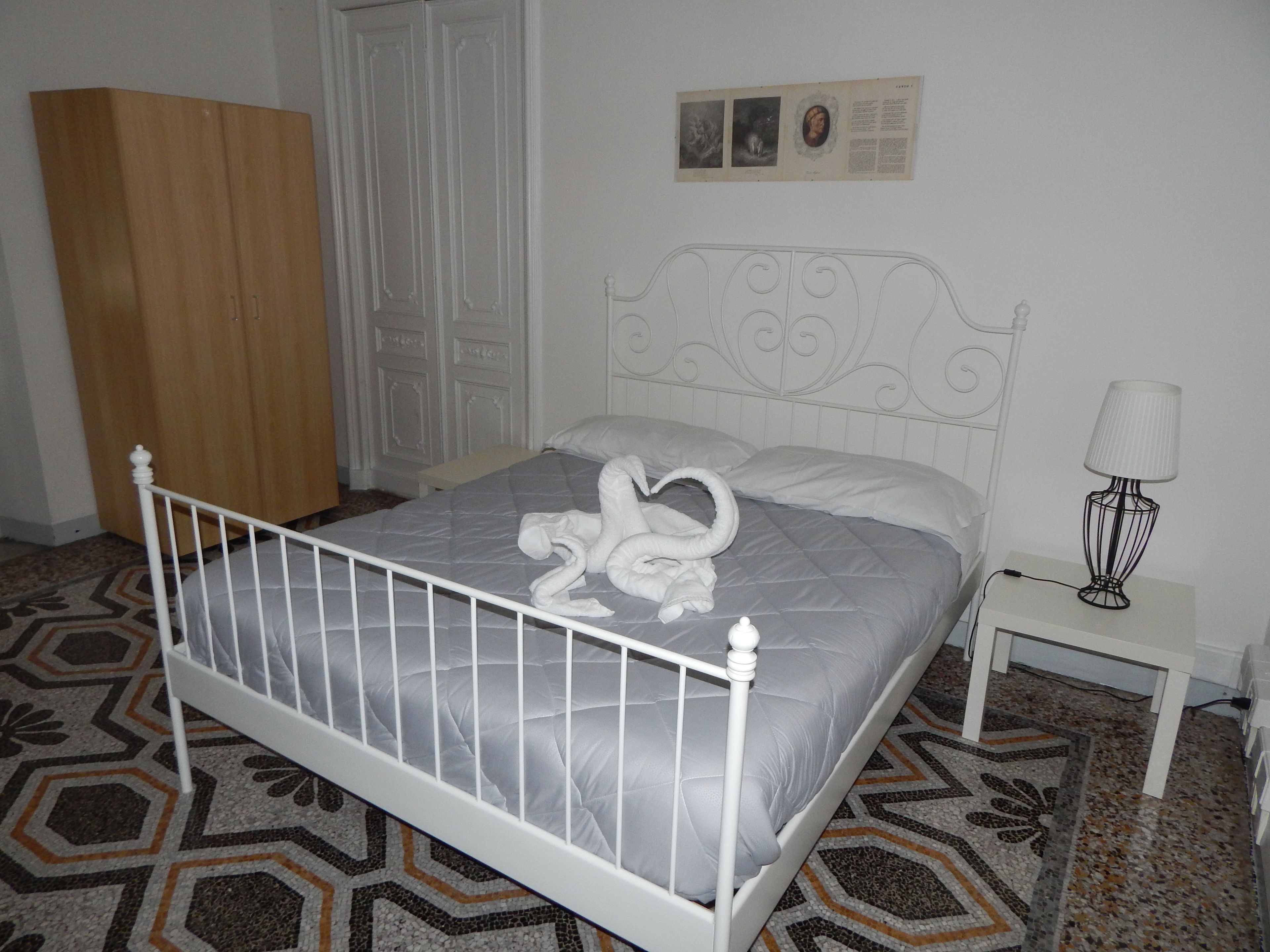 A neatly made bed with a swan-shaped pillow arrangement, a bedside table with a lamp, and a patterned floor.