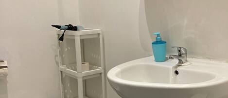 Casa de banho com lavatório pedestal branco, bidé e estante branca.