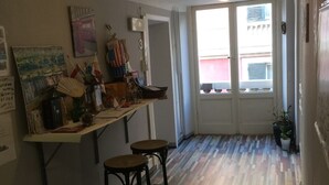 A kitchen with a wooden floor, two stools, a counter with various items, and a door leading outside. - Guest House Roma (Genoa)