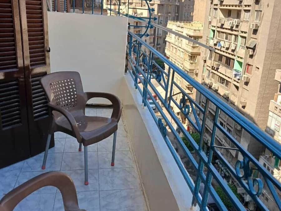 Un balcón con dos sillas de plástico, una baranda metálica y vistas a una zona urbana muy poblada.