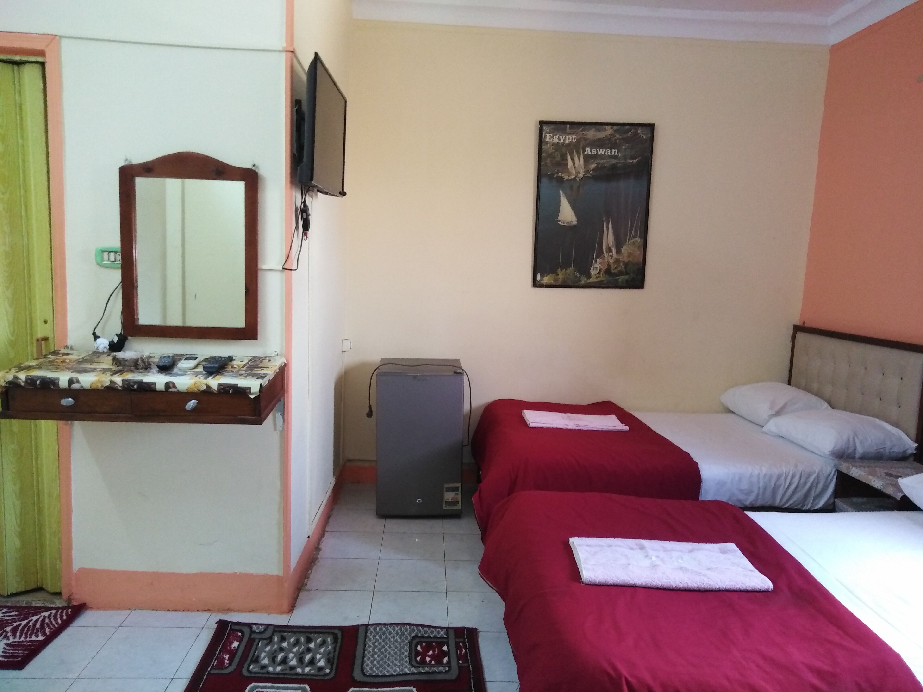 Habitación de hotel con dos camas, un televisor montado en la pared, un escritorio pequeño con un espejo y un cartel de Egipto.
