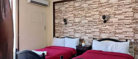 Un dormitorio con dos camas, una pared de piedra, un equipo de aire acondicionado y una mesita de noche con lámpara.