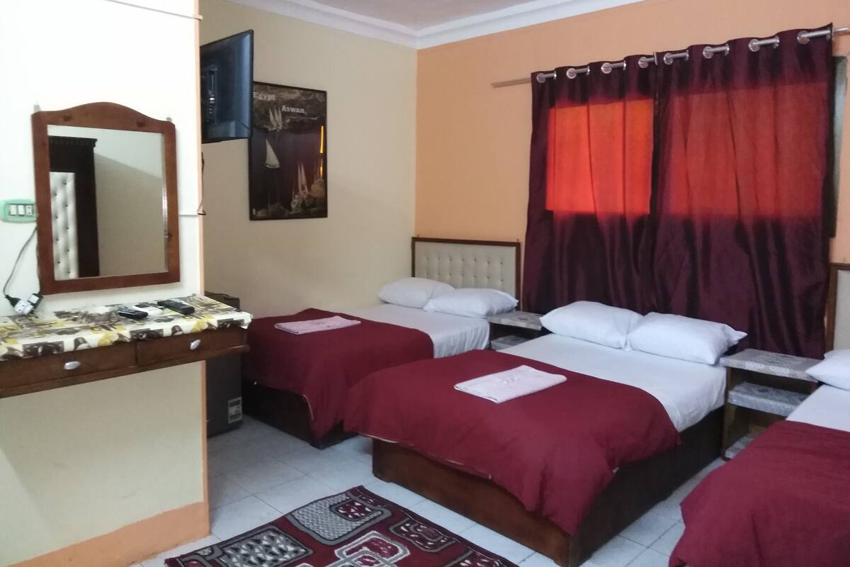 A hotel room with two beds, a mirror, a painting, and a red curtain.