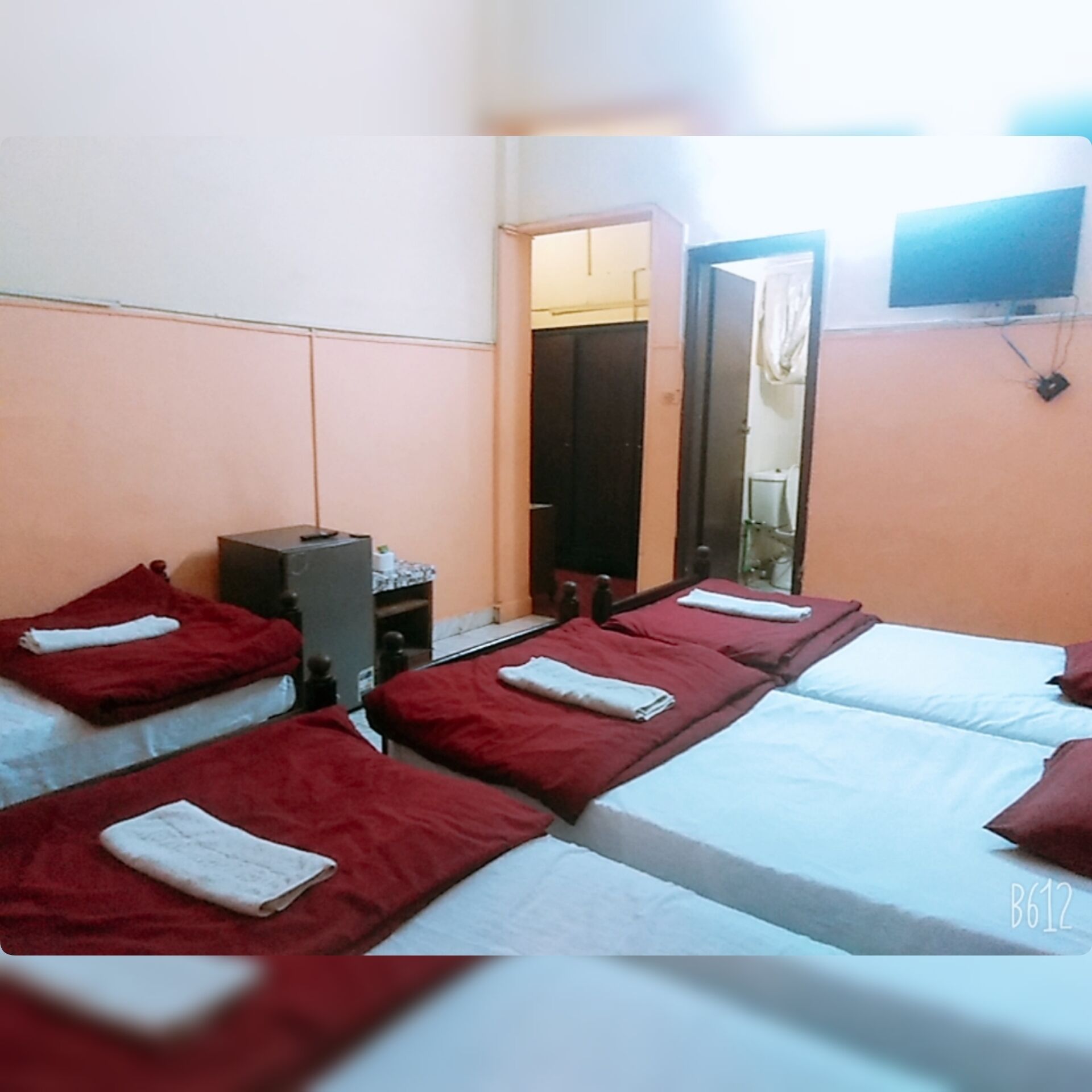 Une chambre d’hôtel avec quatre lits disposés en rangée, un bureau avec une chaise, un téléviseur fixé au mur et un miroir.