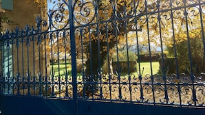 A wrought iron fence with intricate designs, a stone wall, and a tree with yellow leaves in the background. - L'Estancat (Pardies-Pietat)