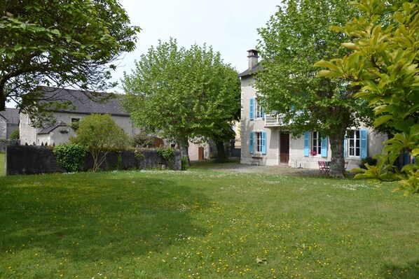 A courtyard with a grassy lawn, a stone wall, and a building with blue shutters. - L'Estancat (Pardies-Pietat)