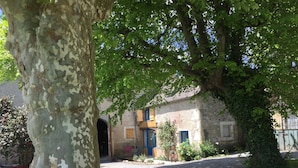 A rustic stone building with a gravel driveway and a large tree in the foreground. - L'Estancat (Pardies-Pietat)