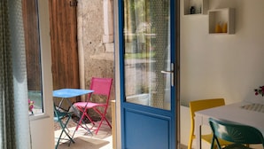 An open door leading to a patio with a table and chairs, a blue-framed glass door, and a hanging light fixture. - L'Estancat (Pardies-Pietat)
