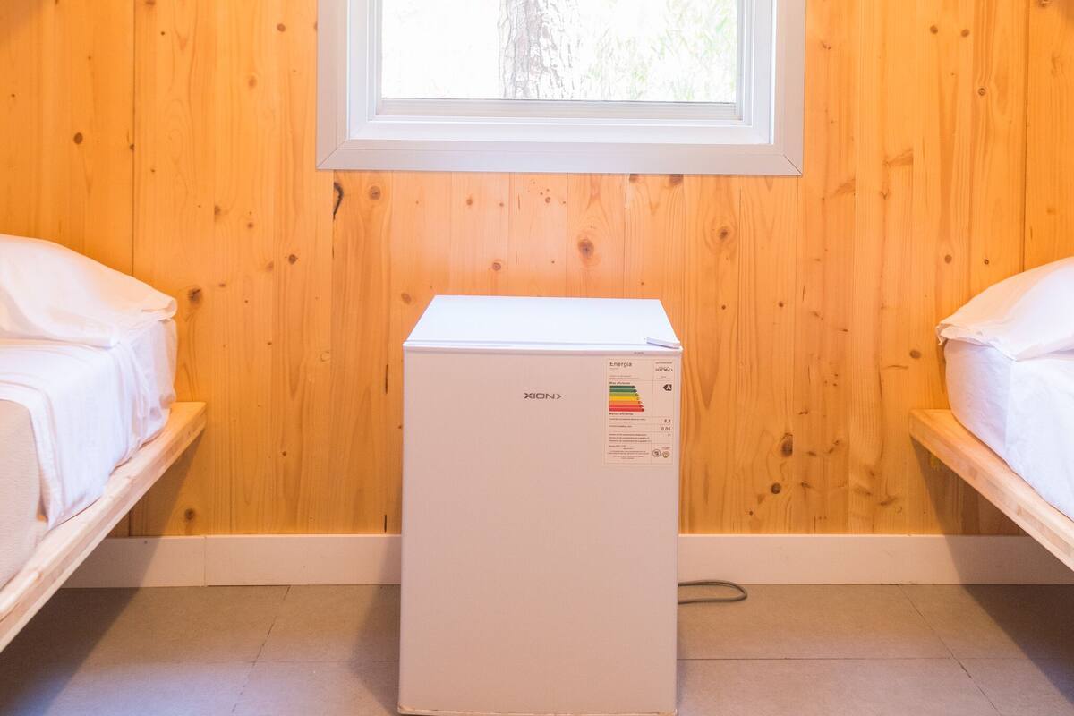 Una stanza con pareti in legno, una finestra, un letto e un elettrodomestico bianco.
