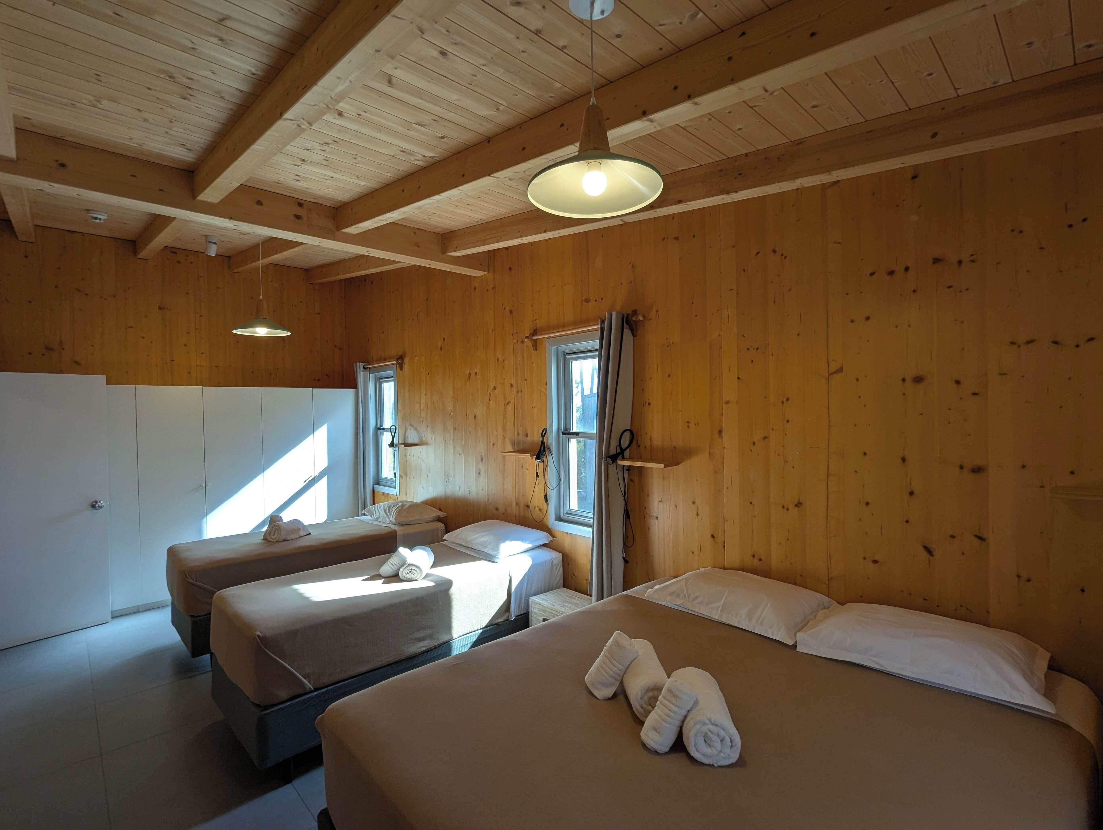 A wooden cabin with two beds, a kitchenette, and a large window.