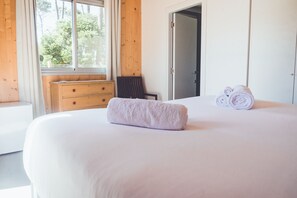 Un dormitorio con una cama grande, un aparador de madera, una silla y una ventana con vistas a árboles.
