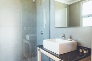 Un baño moderno con cabina de ducha de vidrio, un lavamanos blanco y un espejo grande.