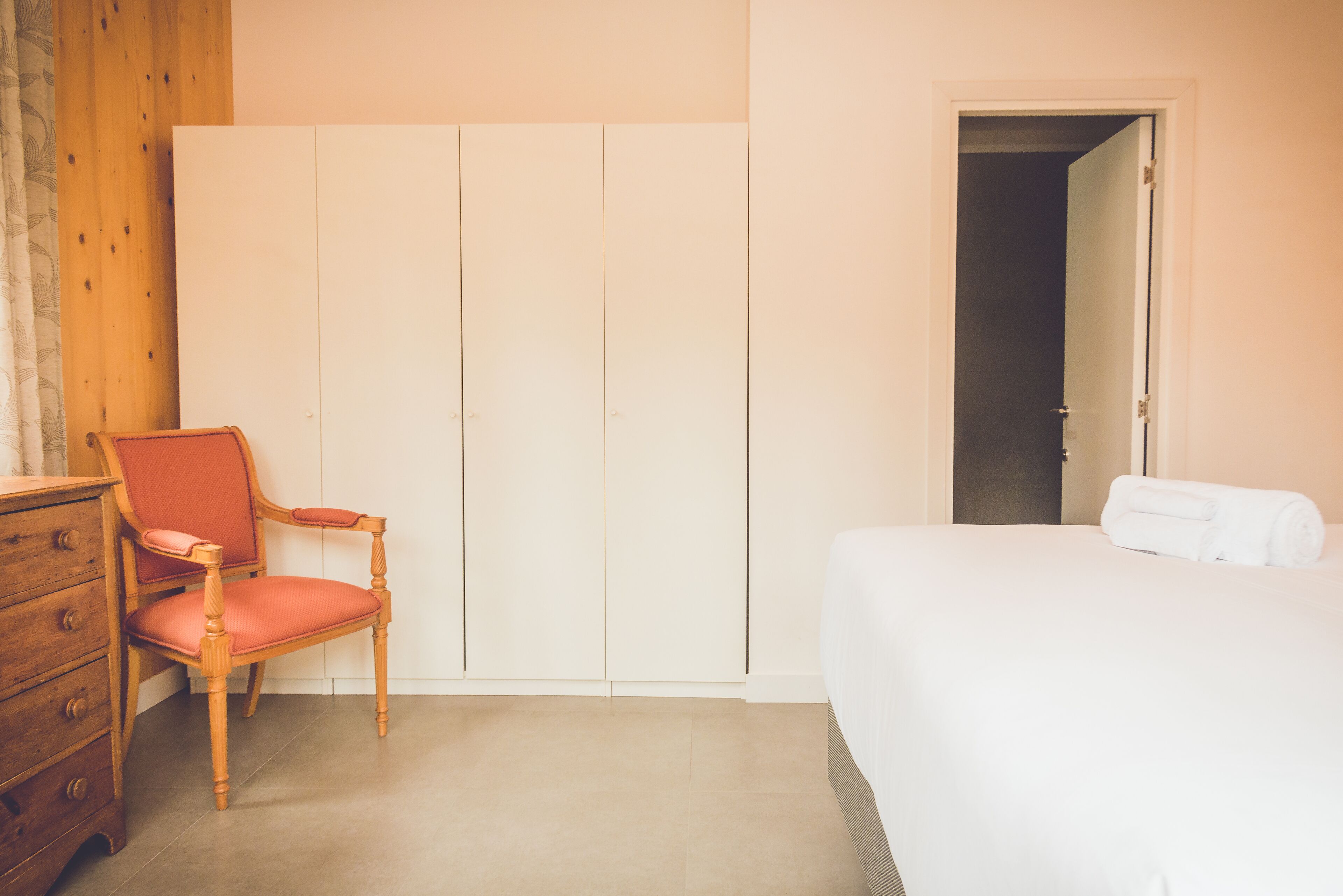 Un dormitorio con cama, una silla de madera, cómoda y armario.