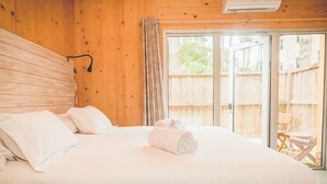 Camera da letto con un ampio letto, lenzuola bianche, una testiera in legno e una porta scorrevole in vetro che dà su una zona esterna con recinzione in legno.