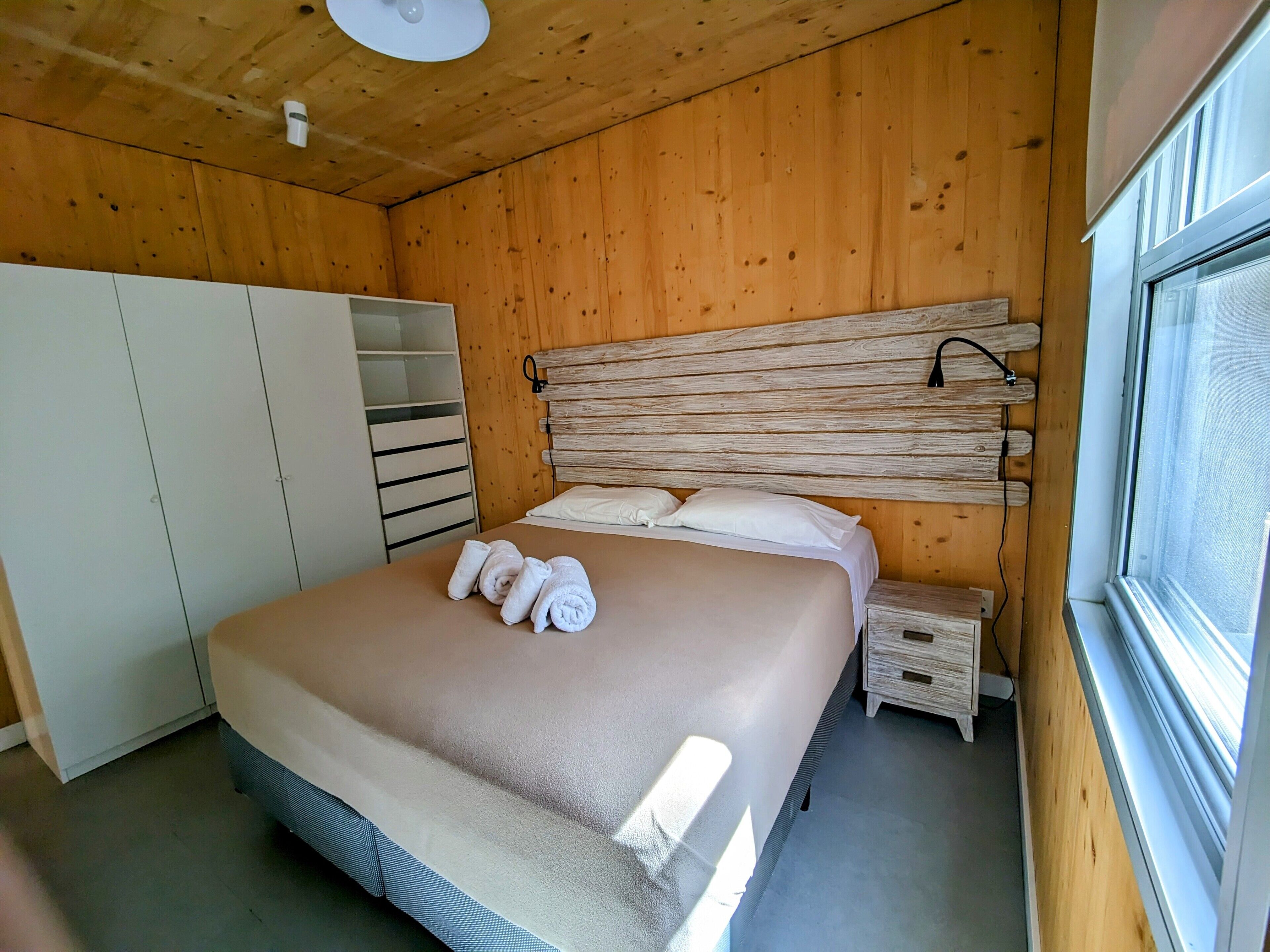 Una habitación con paneles de madera, una cama, un armario y una ventana.